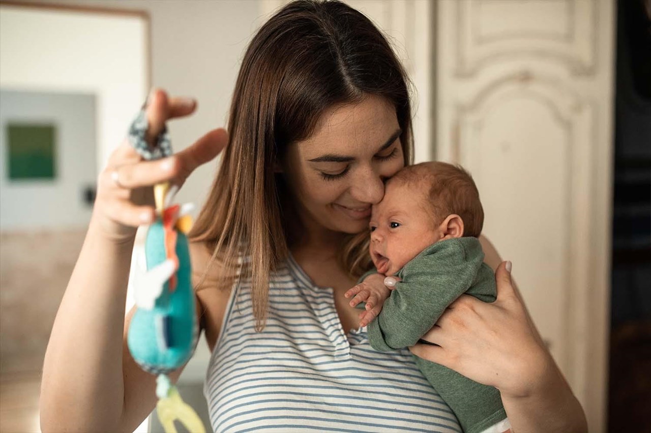 Eine junge Frau mit längeren braunen Haaren hält ein Baby auf dem Arm.