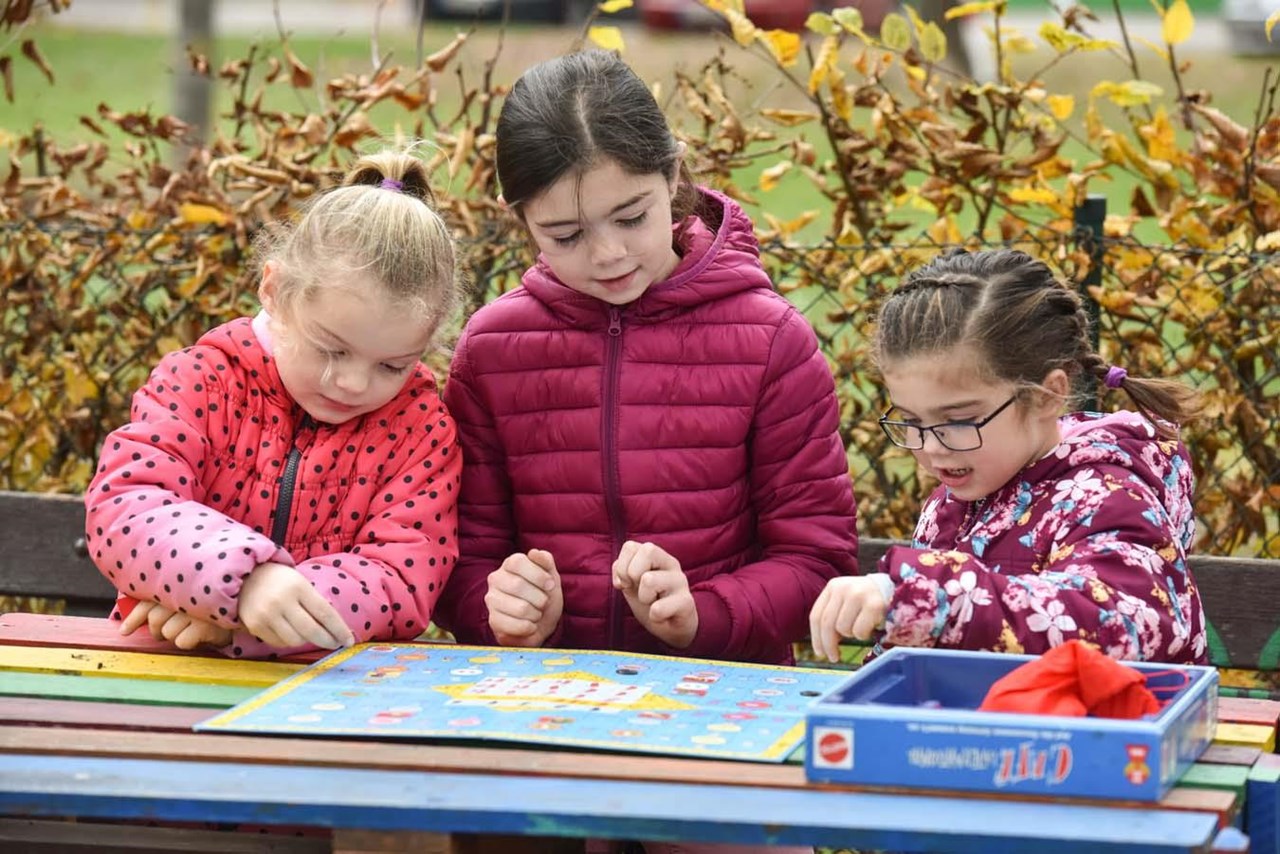 Drei kleine Mädchen spielen ein Brettspiel im Grünen