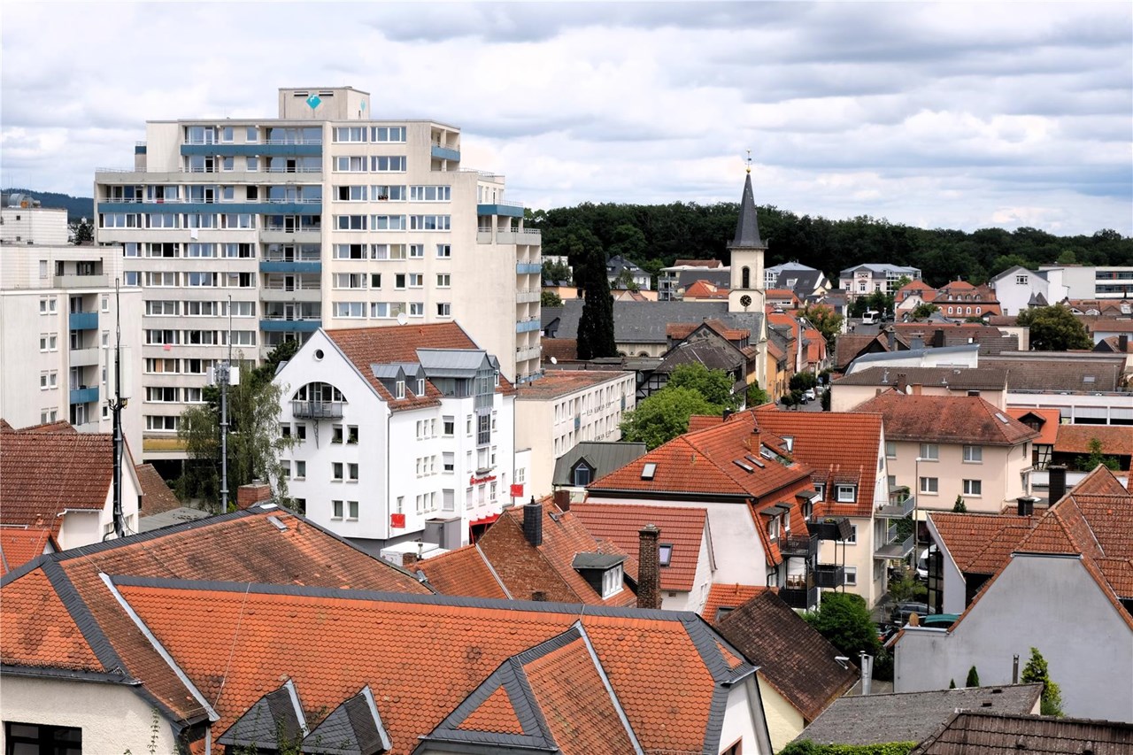 GPT  Stadtbild einer deutschen Stadt mit modernen Wohngebäuden, roten Ziegeldächern und einer Kirche mit Glockenturm im Hintergrund.
